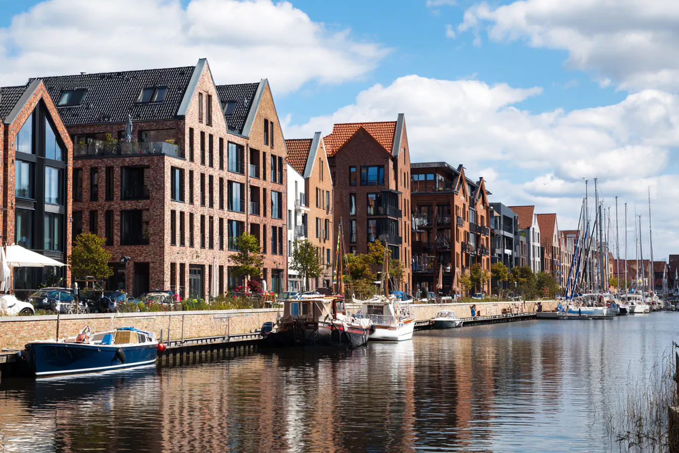 Moderne Backsteinhäuser am Wasser mit Segelbooten und Yachten im Hafen.